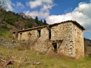 Bulutlar ile mavi gökyüzü altında terkedilmiş yıkılmış köy evi.