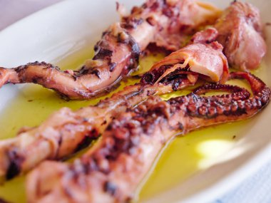 Haşlanmış ahtapot beyaz tabakta yağ ile servis.