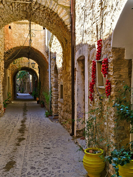 Narrow alley at the medieval castle village of Mesta in Chios island , Greece. Cherry tomatoes bunches hanging from the stone wall to dry.
