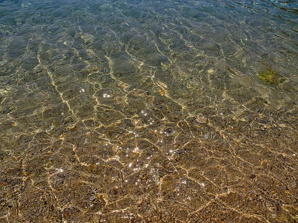 Acqua cristallina da vicino in spiaggia sabbiosa, luce del sole che riflette — Foto Stock