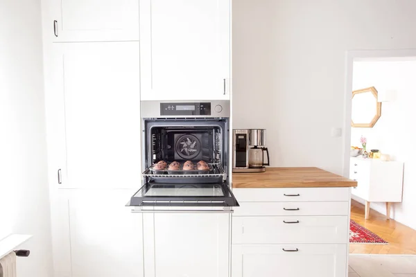 Muffins en una bandeja para hornear en el horno en una cocina blanca brillante en estilo rural moderno — Foto de Stock