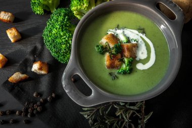 Patates ve vegan siyah arka plan, üstten görünüm üzerinde koyu ahşap tahta üzerinde bir kapta krem ile bahar Detoks brokoli yeşil krem çorbası. Temiz beslenme, diyet, vegan, vejetaryen, sağlıklı gıda kavramı