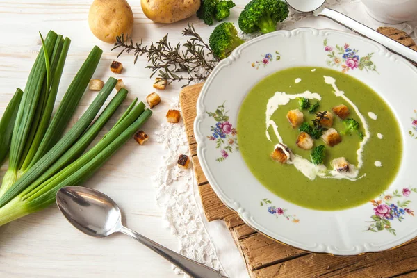 Spring detox broccoli green cream soup with potatoes and vegan cream in bowl on bright wooden board over white background, top view. Clean eating, dieting, vegan, vegetarian, healthy food concept