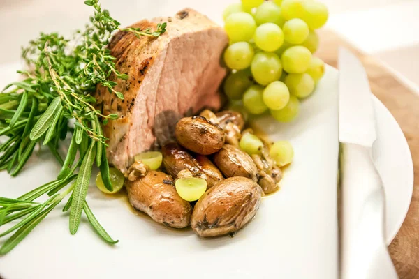 Lezzetli bir parça closeup domuz omuz kavrulmuş sarımsak, üzüm, incir ve taze biberiye ile kavrulmuş.