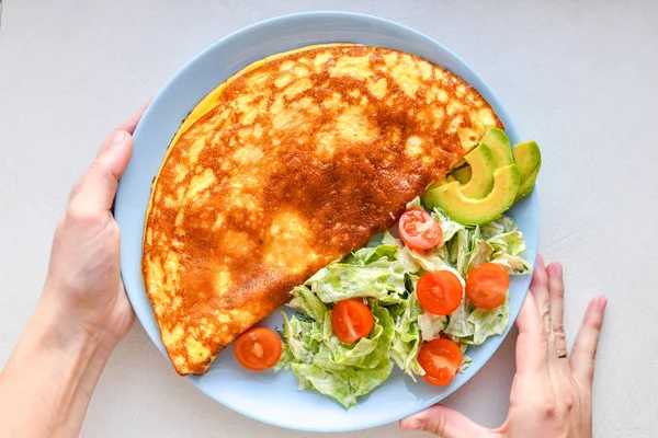 fried eggs with vegetables. hands in the frame. Vegetable omelet on a blue plate on a white table, top view