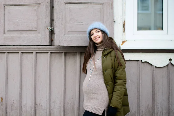 Warmly dressed pregnant girl Beautiful pregnant woman dressed in gray knitted sweaters, hat, scarf and jeans, holding pink cups with hot tea and walking — Stock Photo, Image