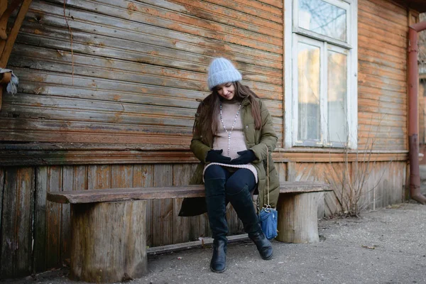 Fille enceinte sur le banc. Une jeune fille enceinte est assise sur un banc. Le concept du début de l'automne et la chute des feuilles et le repos dans le parc et dans la nature. habiller chaudement pendant la grossesse — Photo