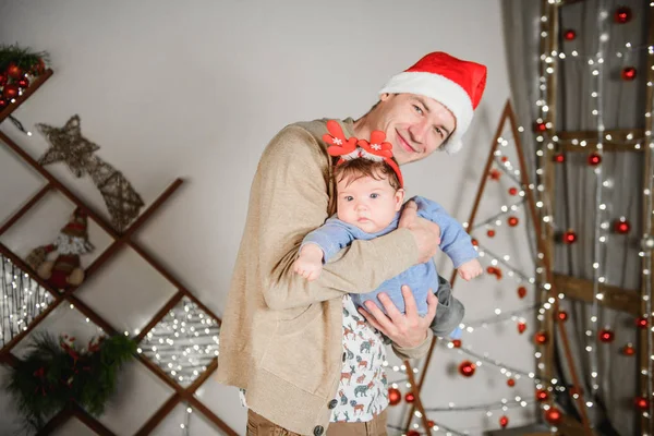 Baba ve oğul Noel ağacında kucaklaşıyorlar. Mutlu bir çocuk ve babası çerçeveye bakıyorlar. Baba oğluyla Noel'de kucaklaşmak. ve eğlenin. kafasına boynuzları. Yeni Yıl şapkası. — Stok fotoğraf