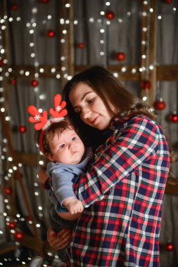 Noel ağacında anne ve bebek kucaklaması. Mutlu bebek ve annesi çerçeveye bakıyorlar. Noel'de oğluyla birlikte anne kucaklıyor. ve eğlenin. yeni yıl için yenidoğan bebek.