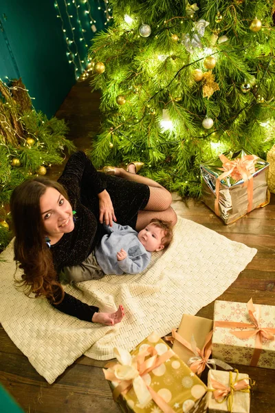 Mamãe e bebê abraçam na árvore de Natal. O bebé feliz e a mãe estão a olhar para a moldura. Mãe com o filho a abraçar-se no Natal. e diverte-te. bebê recém-nascido para o ano novo . — Fotografia de Stock