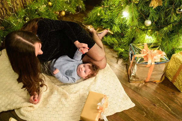 Mamãe e bebê abraçam na árvore de Natal. O bebé feliz e a mãe estão a olhar para a moldura. Mãe com o filho a abraçar-se no Natal. e diverte-te. bebê recém-nascido para o ano novo . — Fotografia de Stock