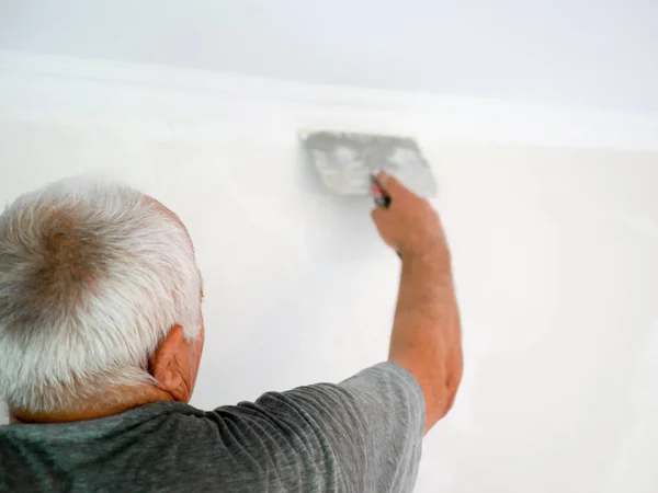 man with a spatula. gray-haired man makes repairs at home. alignment of walls. wholesale developer. back view. Man plastering wall with putty-knife, close up image. Fixing wall surface and preparation