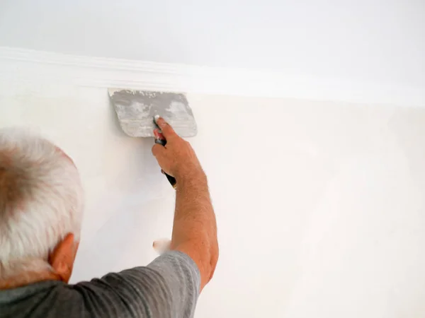 Uomo con una spatola. uomo dai capelli grigi fa riparazioni a casa. allineamento delle pareti. sviluppatore all'ingrosso. vista posteriore. Uomo muro intonacatura con stucco-coltello, immagine da vicino. Fissaggio superficie della parete e preparazione — Foto Stock