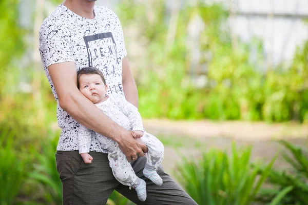 A newborn baby in the arms of his father. Portrait of a young happy man holding his newborn sweet baby dressed in white clothes. Young father hugging his child with love and care, smiling. on the stre — Stock Photo, Image