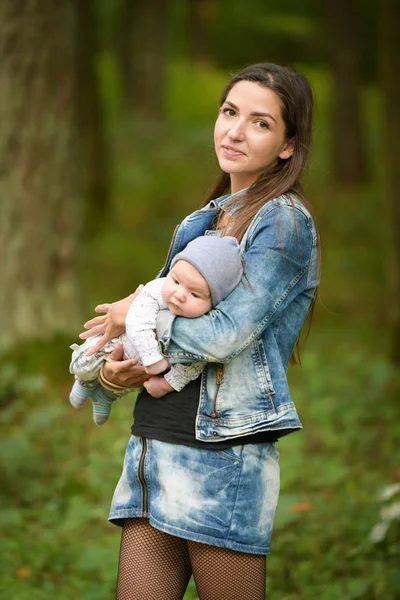 Yeni doğmuş bebeğiyle dışarıda mutlu bir anne. Uzun saçlı ve kot ceketli genç ve şık bir anne yaz parkında küçük tatlı kızıyla oynuyor. — Stok fotoğraf
