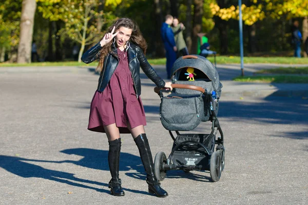 Portrait of mom with a stroller. Portrait of a beautiful young woman pushing a stroller in a park. happy walk with a child