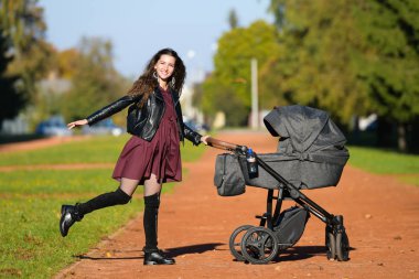Anneyi bebek arabasıyla gezintiye çıkarmış. Parkta bebekle yürüyen genç bir anne. Güzel bir gülümseme ve keyifli bir ruh hali, hayattan memnun..