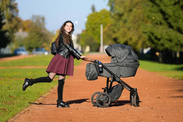 Anneyi bebek arabasıyla gezintiye çıkarmış. Parkta bebekle yürüyen genç bir anne. Güzel bir gülümseme ve keyifli bir ruh hali, hayattan memnun..