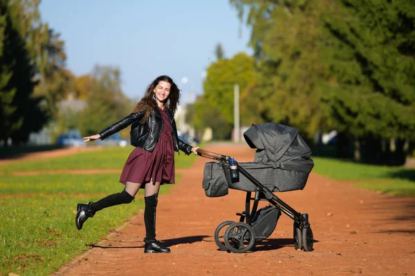 Portret mamy z wózkiem. Portret pięknej młodej kobiety pchającej wózek w parku. szczęśliwy spacer z dzieckiem — Zdjęcie stockowe