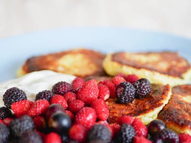 Böğürtlenli peynirli kek. Ve ekşi krema. Peynirli kekler beyaz tabakta bir sürü taze böğürtlenle servis edilir. Gurme kahvaltı - peynirli kek, ahududulu krep, çilek, yaban mersini