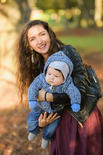 Annesinin kollarında komik bir bebek. Oğlunu kollarına almış çekici genç bir anne. Mutlu bir anne ve bebeğin gülüşünün portresi. Genç anne bebeğini kucağında tutuyor. — Stok fotoğraf