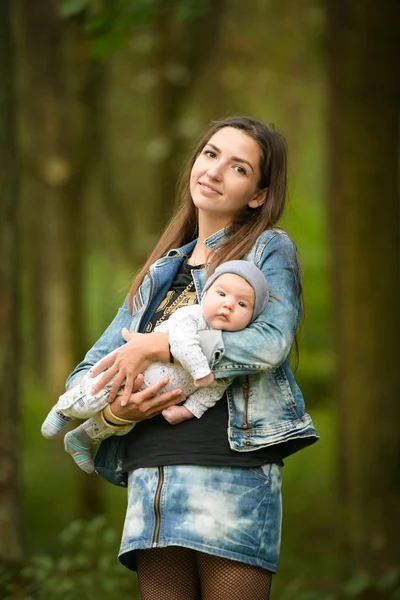 Sokakta bebekle dolaşan genç bir annenin portresi. Bahar sokağında gülümseyen genç bir annenin ellerinde. — Stok fotoğraf