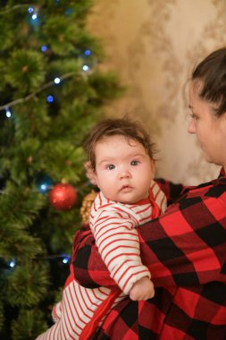 Noel ağacının yanında çocuklu bir anne. Ağacı topla ve tatil için hazırlan. Sevimli, açık renk saçlı, güzel annesi kalın kazaklar giyen ve gülümseyen bir kızın yarım boy portresi.