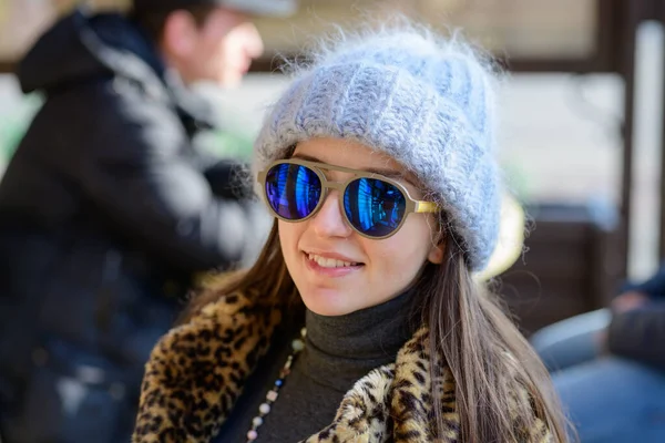 A girl in blue glasses and a warm plump gray hat posing outside in the cold season. portrait of a beautiful girl in glasses — Stock Photo, Image