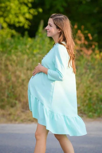 Mädchen hält einen schwangeren Bauch. Schwangere vor dem Hintergrund der Natur, warmes Wetter. — Stockfoto