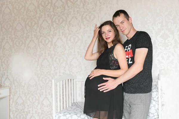 Espera um bebé ao lado do berço. Retrato de um lindo jovem casal ao lado de um berço em um berçário. futuros pais . — Fotografia de Stock