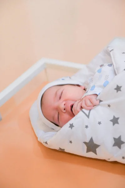 Baby in the hospital, lying on the sofa, wrapped in a blanket, discharge of the child from the maternity hospital, birth of the child. Sleeping cute newborn baby wrapped in a baby blanket, in an acryl