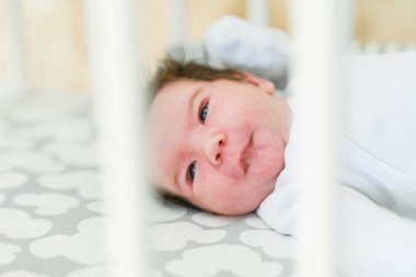 Beşikteki bebek. Yeni doğmuş erkek bebek yatakta. Beyaz örgü battaniyenin altında uyuyan yeni doğmuş bir çocuk. Çocuklar uyur. Çocuklar için yatak. Yatakta bebek şekerlemesi. Doğumdan kısa bir süre sonra sağlıklı küçük bir çocuk. Kablo