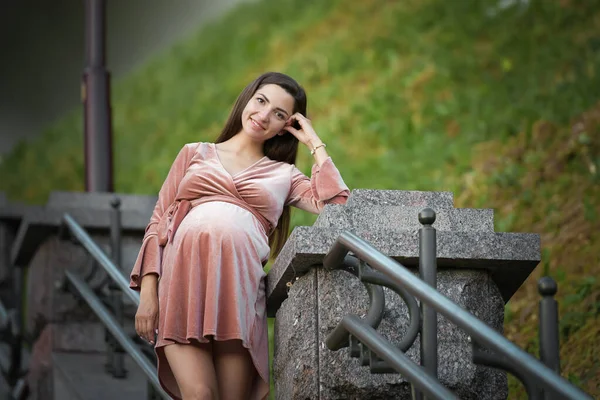 Pregnant girl posing on the stairs. brunette in a velor dress. in the open air — Stockfoto