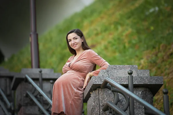 Pregnant girl posing on the stairs. brunette in a velor dress. in the open air — Stockfoto