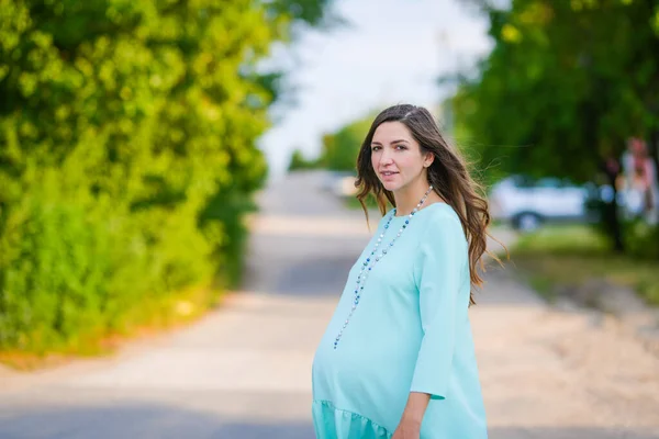 Schwangere in türkisfarbenem Kleid. Schwangere im Tagkleid schlendert durch den Park. lächelt das Mädchen. Bequeme Kleidung für Schwangere. — Stockfoto