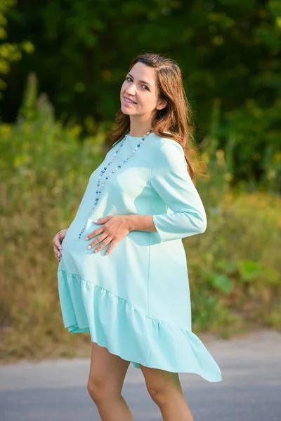 Pregnant girl hugs her pregnant belly. Happy pregnant woman is embracing belly on nature, outdoors — Stockfoto