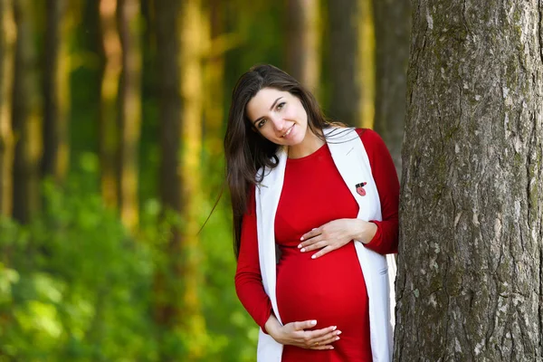 Gravid flicka i röd klänning. Porträtt av vacker gravid kvinna i röd klänning i den blommande vårparken — Stockfoto