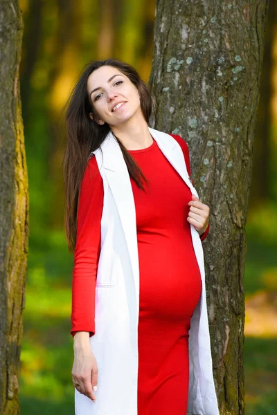 Incinta con una vestaglia bianca. Ragazza incinta in un cappotto bianco passeggiando nella natura — Foto Stock