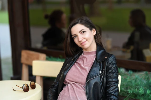 Chica embarazada sentada en un café. Atractiva morena embarazada sentada en un sofá en una terraza cafetería — Foto de Stock