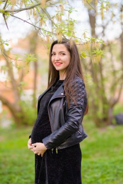 Çiçekli parktaki hamile esmer kadın. Koyu renk elbiseli esmer, çiçek açan elma bahçesinde poz veriyor.