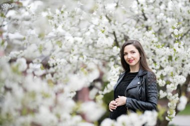 Çiçekli parktaki hamile esmer kadın. Koyu renk elbiseli esmer, çiçek açan elma bahçesinde poz veriyor.
