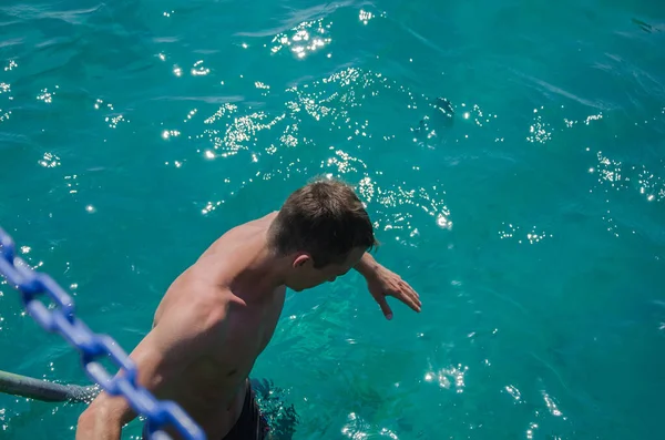 Adam denize gidiyor. Erkek bir yüzücü, gün batımında iskele çitini tutarken, çıplak ayakla aşağıya, denize doğru görünür. Yüzme, yaz ve rahatlama kavramları — Stok fotoğraf