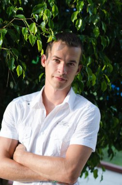 Yeşillik arka planında beyaz gömlekli yakışıklı bir adam. Yeşil yapraklı genç adam şaşırdı..