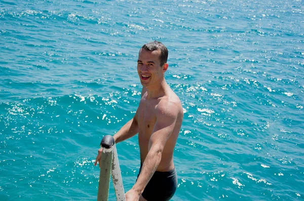 这家伙出海去了。 一名男性游泳者赤脚从腰部一直游到大海，夕阳西下时手握码头围栏。 游泳、夏天和放松的概念 — 图库照片