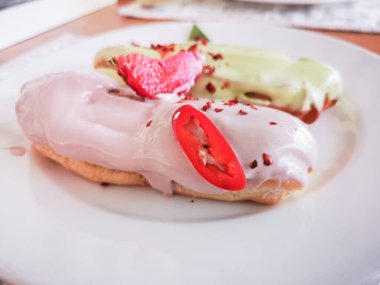 Beyaz bir tabakta renkli jöleli ekler. Ev yapımı ekekler. Geleneksel ekler, klasik profesyoneller, eklairlerin Fransızcası. Fıstık, vanilya, jöleli çilek. Tahta bir masada.