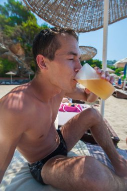 Plajda plastik bardaktan bira içen bir adam. Plajda plastik cam bira içen adam.