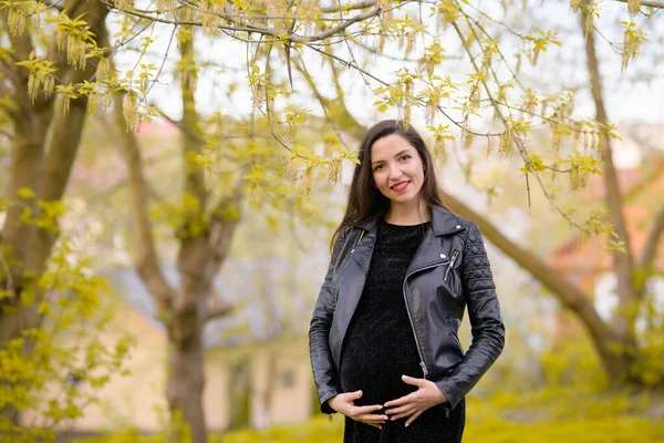 Pregnant girl in the garden. Pregnant woman feeling happy with new life at garden home while take care of her child. The young expecting mother holding baby in pregnant belly. Maternity prenatal care — Stockfoto