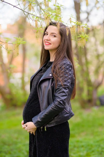 Pregnant girl in the garden. Pregnant woman feeling happy with new life at garden home while take care of her child. The young expecting mother holding baby in pregnant belly. Maternity prenatal care — Stockfoto