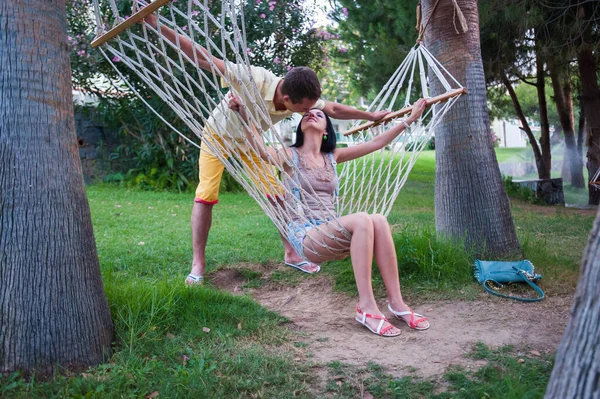 Meisje en jongen kussen op vakantie. Hangmat liefde. Gelooide jongeman kust een mooie brunette op de achtergrond van palmbomen. Rust en rust. Huwelijksreis concept. — Stockfoto