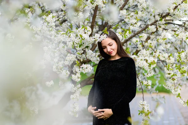 Çiçekli bahçede hamile bir kız var. Siyah elbiseli güzel hamile kız çiçekli bir bahçede duruyor. — Stok fotoğraf